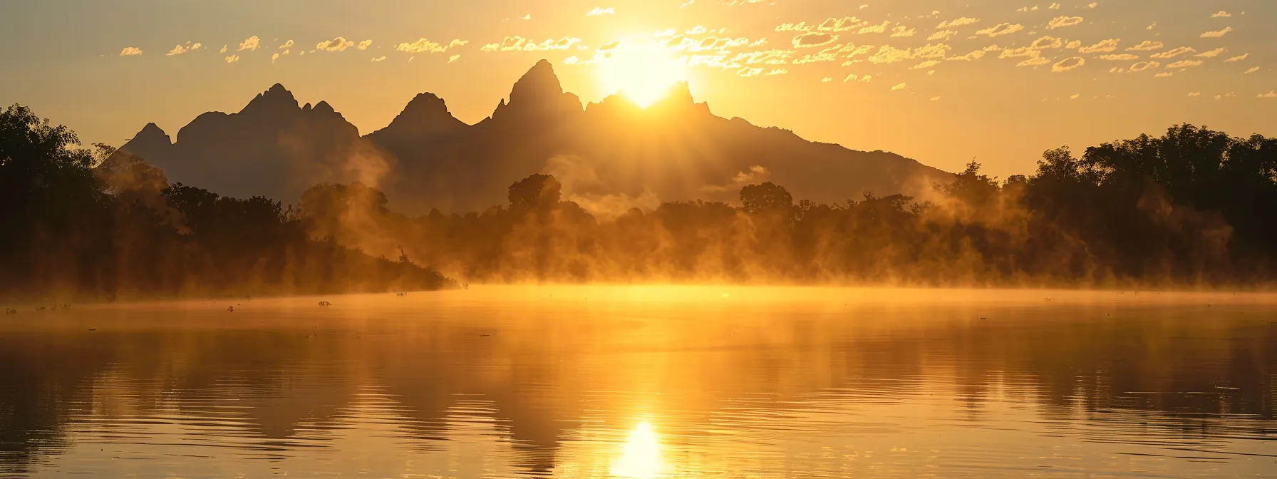 a breathtaking sunrise casts a golden hue over a tranquil lake, with mist rising from the water's surface and silhouettes of majestic mountains reflecting in the stillness.