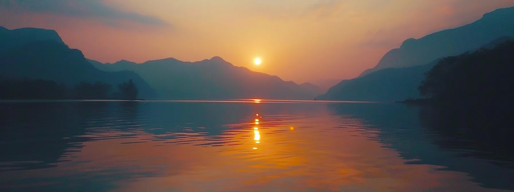 a breathtaking sunset casts vibrant hues of orange and pink across a tranquil lake, while silhouetted mountains loom majestically in the background, creating a serene and captivating atmosphere.