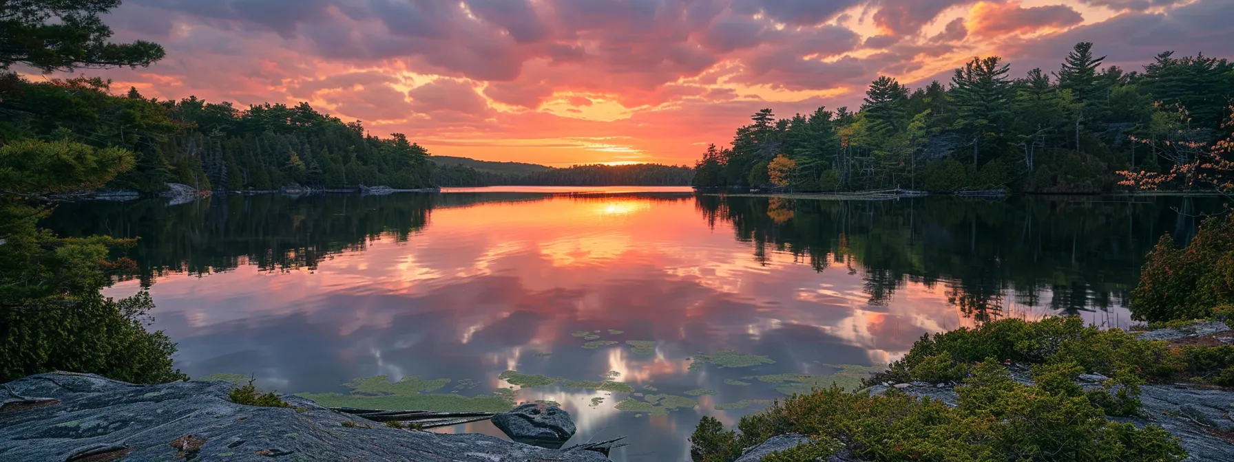 a tranquil sunrise paints the sky in vibrant hues of orange and pink over a serene lake, reflecting the colorful spectacle on its calm surface, surrounded by lush, green foliage.