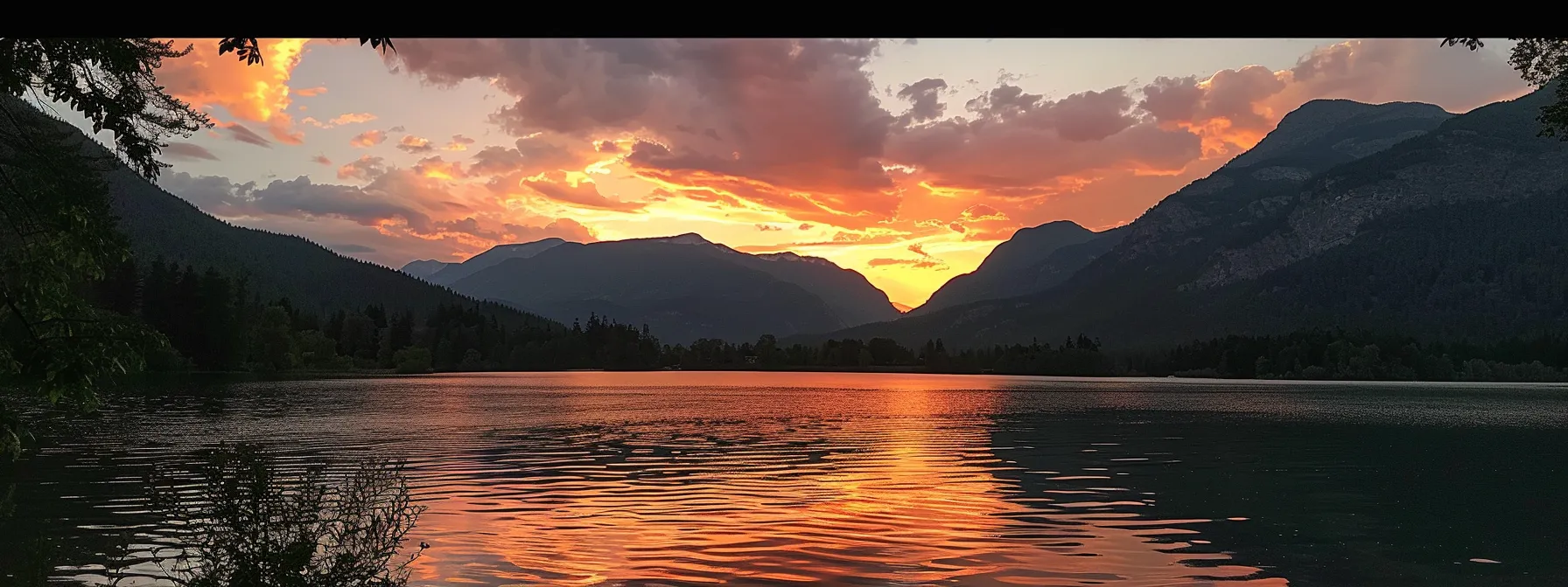 a vibrant sunset casts a golden glow over a tranquil lake, reflecting the fiery colors of the sky while silhouetted mountains rise majestically in the background.