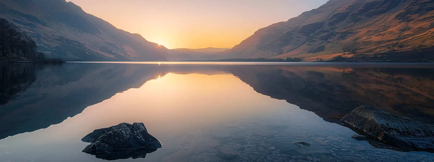 a vibrant sunset casts a warm golden hue over a serene lake, reflecting the dramatic silhouettes of distant mountains under a clear sky.