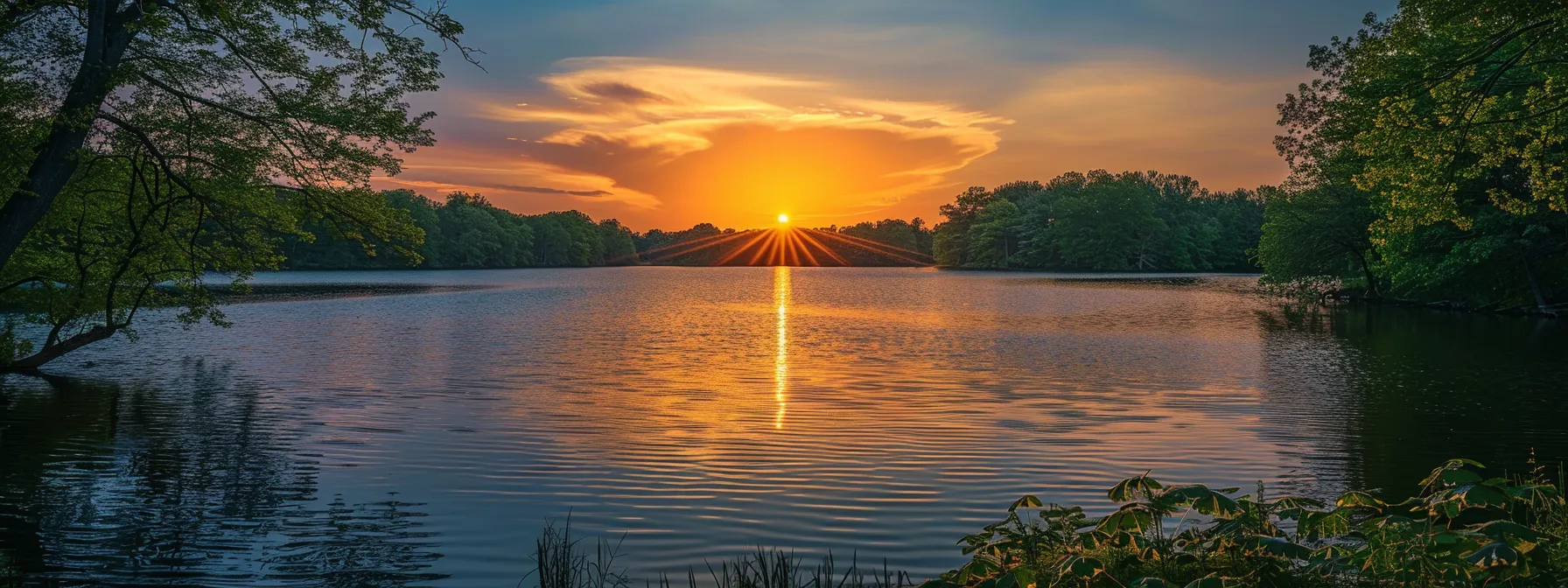 a vibrant sunset casts a warm golden glow over a tranquil lake, reflecting the fiery hues of the sky and surrounded by lush, green trees.