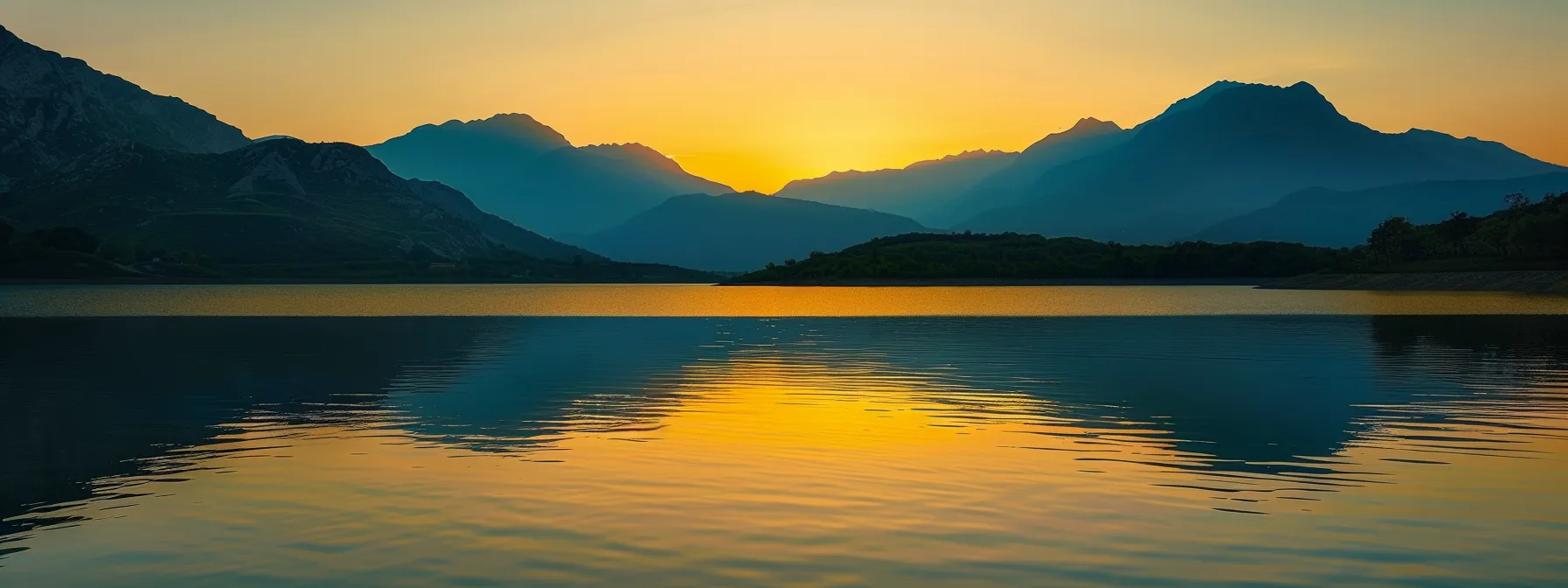 a vibrant sunset casts a golden hue over a tranquil lake, reflecting the silhouette of majestic mountains under a clear sky, creating a serene and picturesque landscape.