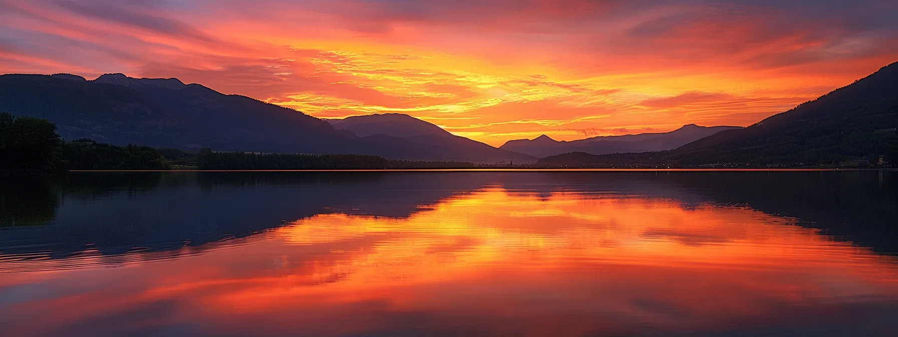 a vibrant sunset casts a golden glow over a serene lake, reflecting the fiery colors of the sky while silhouetted mountains loom majestically in the background.