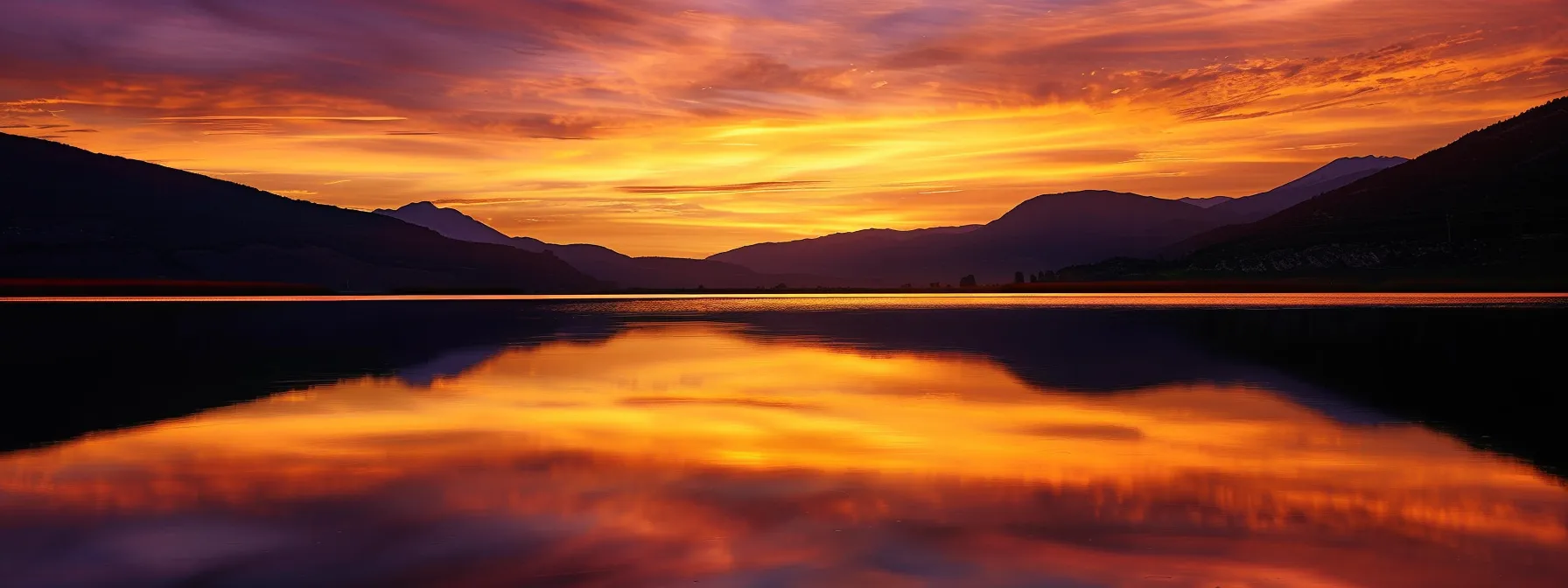 a vibrant sunset casts a golden hue over a serene lake, reflecting the dramatic silhouettes of distant mountains under a sky painted with swirling shades of orange and purple.