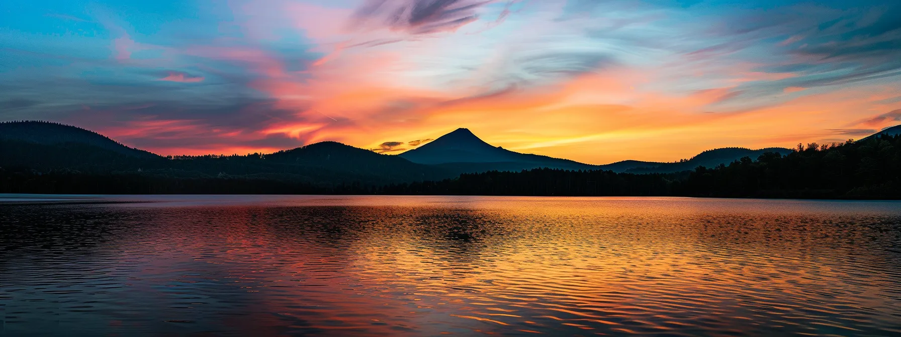 a vibrant sunset casts a warm golden glow over a serene lake, where a solitary silhouette of a majestic mountain rises dramatically against the colorful sky.