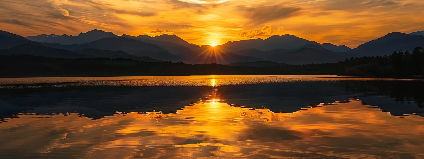 a vibrant sunset casts golden hues over a serene lake, reflecting the dramatic silhouette of towering mountains against a sky painted with wispy clouds.