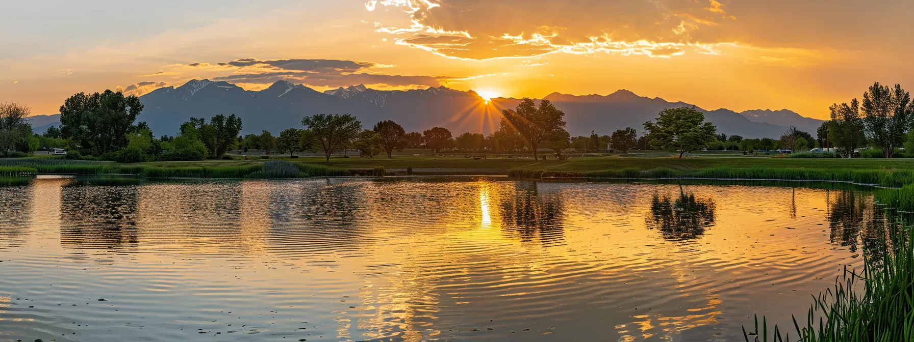 a vibrant sunset casts golden hues over a serene lake, with silhouetted mountains reflecting in the calm water, creating a tranquil and picturesque landscape.